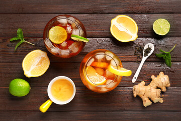Glasses of cold tea with citrus fruit slices, mint leaves and ginger on wooden background