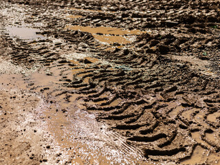 Tire tracks create intricate patterns in wet mud at a rural construction site. Puddles form in the low areas, reflecting the sky. The scene highlights the effects of rain on the terrain