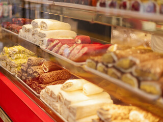 A variety of traditional sweets are neatly arranged in a local shop. The vibrant colors and diverse shapes attract customers in the warm afternoon sunlight
