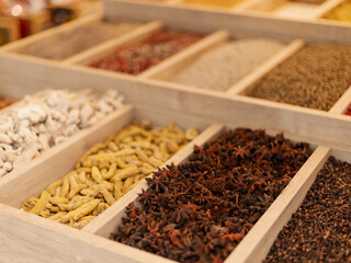 Various spices are organized in wooden trays at a market, showcasing vibrant colors and textures. The scene captures the essence of a bustling marketplace
