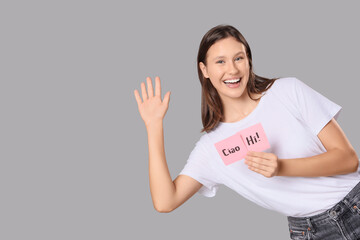 Young woman holding papers with words HI and CIAO on grey background © Pixel-Shot