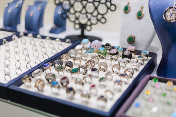 Numerous rings and earrings are arranged on display in a jewelry store. Each piece features unique designs, colorful gemstones, and delicate details, attracting attention from shoppers