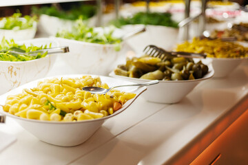 A vibrant buffet spread showcases bowls of pasta, lettuce, and pickles. The bright colors and textures invite guests to create their own delicious meal