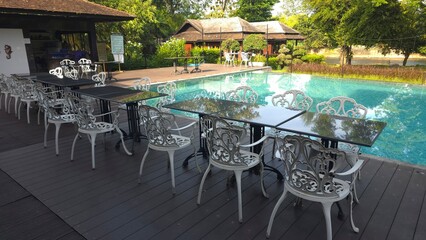 Elegant Outdoor Dining Area with Tables and Chairs by Serene Swimming Pool in Nature