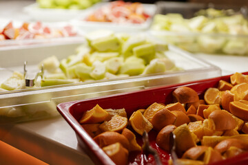 A vibrant selection of fresh fruits is arranged beautifully at a buffet, featuring orange slices, melons, and citrus fruits. The display invites guests to taste healthy options