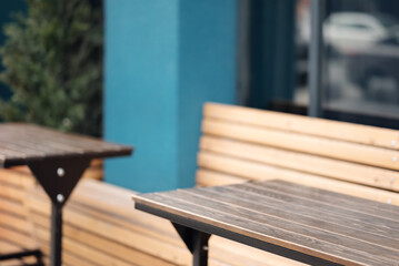 Fototapeta premium Horizontal banner of outdoor wooden tables and benches against blue wall, capturing cozy city cafe design with copy space for text.