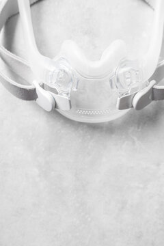 A full face CPAP mask shot over a grey textured background. The mask is used to give therapy to patiences who have been diagnosed with sleep apnea.