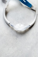 A nasal pillow style CPAP mask shot over a grey textured background. The mask is used to give therapy to patiences who have been diagnosed with sleep apnea.