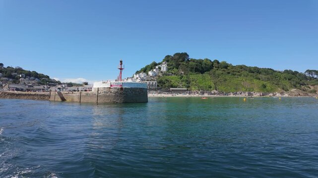 Banjo Pier, in Looe, Cornwall, UK. Shot from a passing poat the camera sees the pier and then Looe beach. Beautiful blue calm waters with a boat wake. 