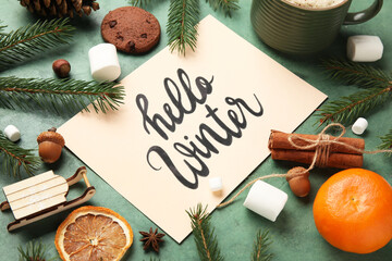 Paper with text HELLO WINTER, treats and Christmas branches on green grunge background