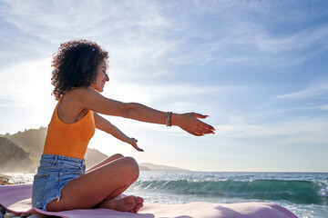 Woman extending arms on beach, embracing nature and freedom, practicing mindfulness at sunset