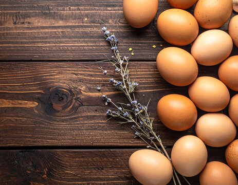 An overhead shot showcases a collection of fresh, brown eggs arranged on a rustic, dark wooden surface. Lavender sprig adds a touch of elegance