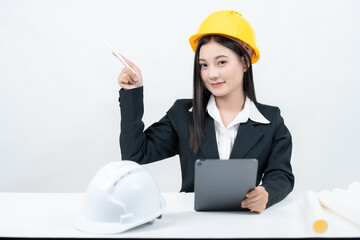 At a desk with a tablet and greenprint, an Asian female engineer is captured in a studio shot with a white background, emphasizing her influence in the industry through active social media presence.