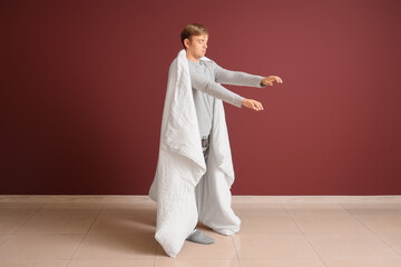 Male sleepwalker in pajamas with blanket near burgundy wall