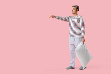 Male sleepwalker in pajamas with pillow on pink background