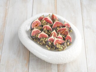 Fresh figs, halved and dipped in chocolate, are presented on a white oval plate. They are sprinkled with chopped pistachios, creating a visually appealing autumn dessert