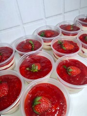 Homemade no bake strawberry cheesecakes in clear plastic cups, topped with fresh strawberries and strawberry compote 