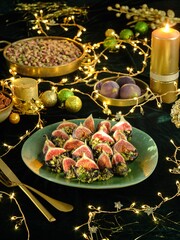 Delicately prepared figs, dipped in chocolate and sprinkled with pistachio, rest on a green platter. Golden cutlery, lit candles, and soft lights create a festive ambiance