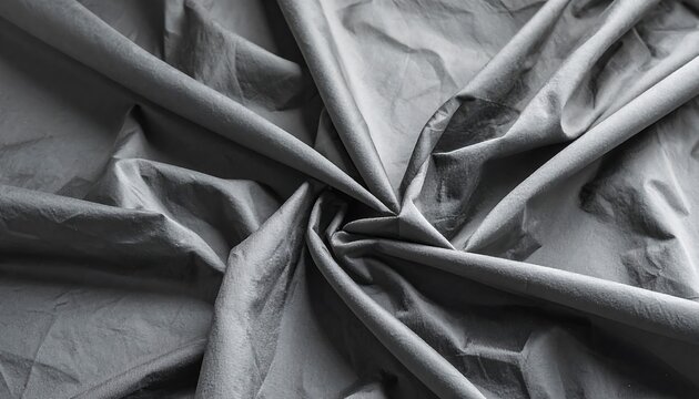 An overhead view showcases draped, matte fabric in gray tones, formed into a spiraling pattern from the center, creating folds and shadows