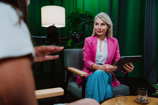 Group of hosts is capturing a live audio broadcast, engaging in a lively, amusing conversation around microphones and a laptop in a professional studio setting