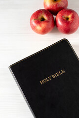 Christian holy bible with red apples on white wooden background. Copy space. Spiritual fruit, studying and reading Scriptures, biblical concept.