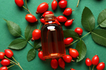 Bottle of cosmetic rose hip oil and berries on green background
