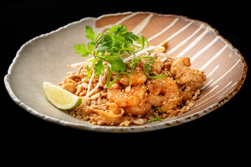 Traditional Pad Thai with chicken, rice noodles, bean sprouts, peanuts, and lime in a ceramic bowl on black background. Authentic Thai cuisine in vibrant, appetizing presentation.