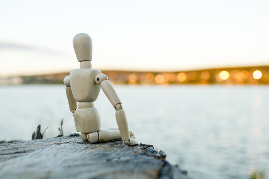 A wooden figure is sitting on a log by a body of water - Powered by Adobe