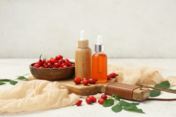 Bottles of cosmetic rose hip oil and wooden bowl with berries on white background