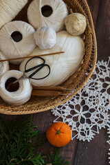 Cozy still life with white yarn, wooden crochet hooks, and stylish scissors in a basket. Minimal natural composition for handmade crafts, eco home decor, and winter DIY projects.