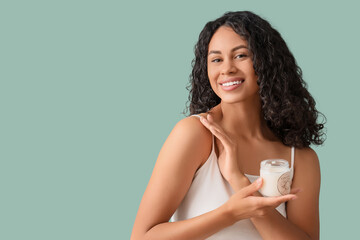 Young African-American woman applying coconut oil to her shoulder on green background