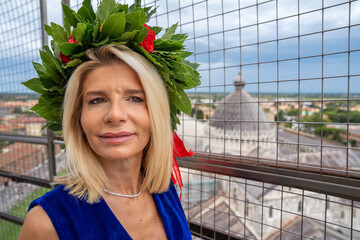 Young woman with graduation laurel crown posing happily on Pisa’s famous tower after ceremony