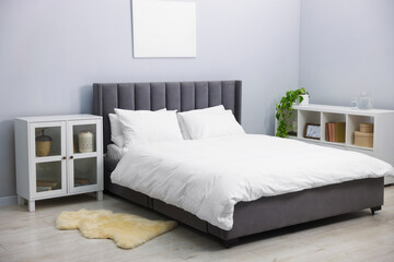 Large bed with linens, shelving unit and cabinet near grey wall in bedroom. Interior design