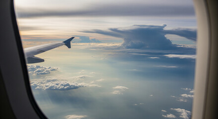 Obraz premium Airplane window view of massive cumulonimbus cloud and wing. A dramatic aerial view from an airplane window captures the stunning sight of a towering cumulonimbus cloud formation