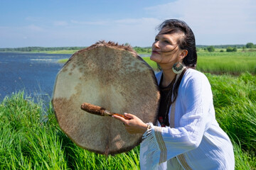 Female shaman in the white dress drumming outdoors