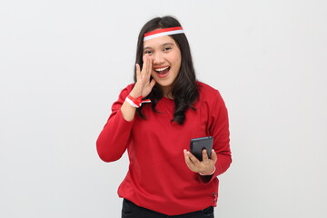 Naklejka premium Indonesian woman with red and white ribbon to celebrate Indonesian independence day holding mobile phone while making hand gestures of announcement or promotional advertisement.