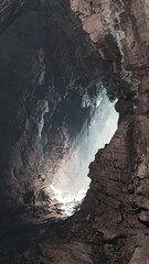 Sunlight streams into a deep cave, illuminating the rocky walls and lush green plants. Shadows dance, creating a mystical atmosphere in this hidden nature gem.