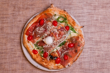 Pizza tradizionale napoletana con prosciutto crudo, mozzarella, rucola, pomodorini e scaglie di formaggio servita in una pizzeria