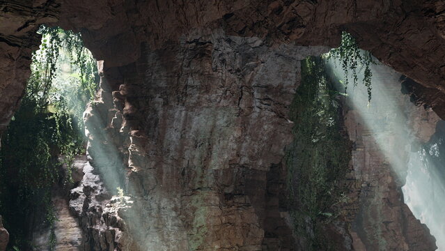 Bright rays of sunlight stream through openings in a rocky cave. Lush green vines cling to the walls, creating a serene and mystical atmosphere in a natural setting.