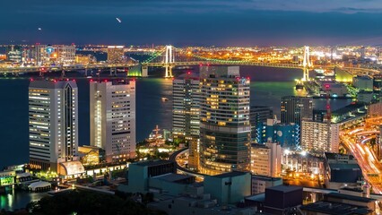 Night view of  waterfront with illuminated Rainbow Bridge and city buildings reflecting, capturing modern skyline and vibrant urban lights