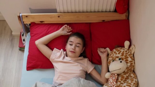 A little girl wakes up, sits up and stretches in bed.