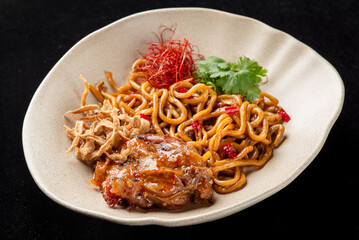 Stir-fried udon noodles with chicken, vegetables, and garnished with cilantro and chili threads on a beige plate. High angle view against a dark background.