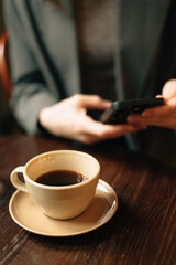 A cup of coffee is on the table, the girl is holding a phone