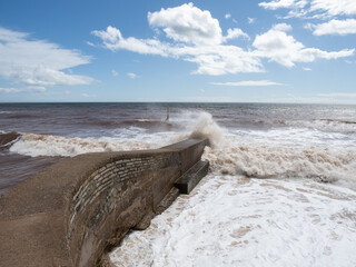 Waves breaking on the shore in Devon with blue sky and fluffy clouds