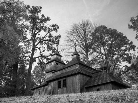 Black and white photo of the Greek Catholic wooden church with three towers in Kožany, Slovakia, a quiet place of faith surrounded by old trees. - Powered by Adobe
