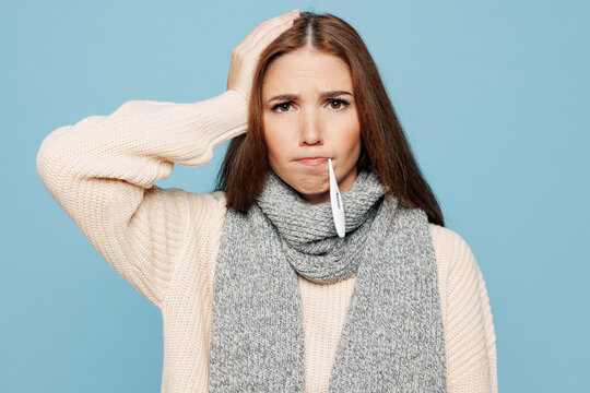 Young sad woman she wear pink sweater scarf hold use thermometer measure temperature isolated on plain blue background studio portrait Healthy lifestyle ill sick disease treatment cold season concept