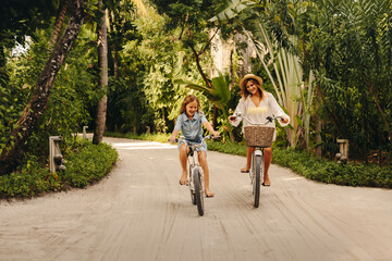 Happy mother and daughter biking at tropical resort island enjoying a sunny day