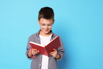 Obraz premium Cute boy with book on light blue background