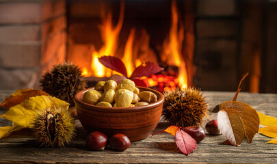 Chestnuts in bowl with autumn leaves warming by a fireplace