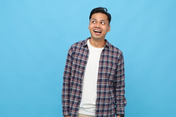 Young asian man, surprised, happy, amazed, wearing casual clothes, glancing sideways at empty space while smiling with funny facial expression, isolated on blue background.